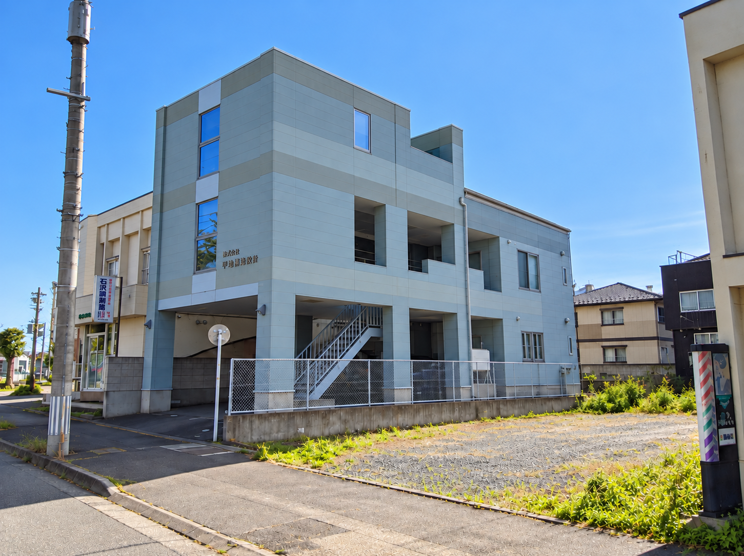株式会社 甲地構造設計の事務所外観。グレーの外壁と社名看板。